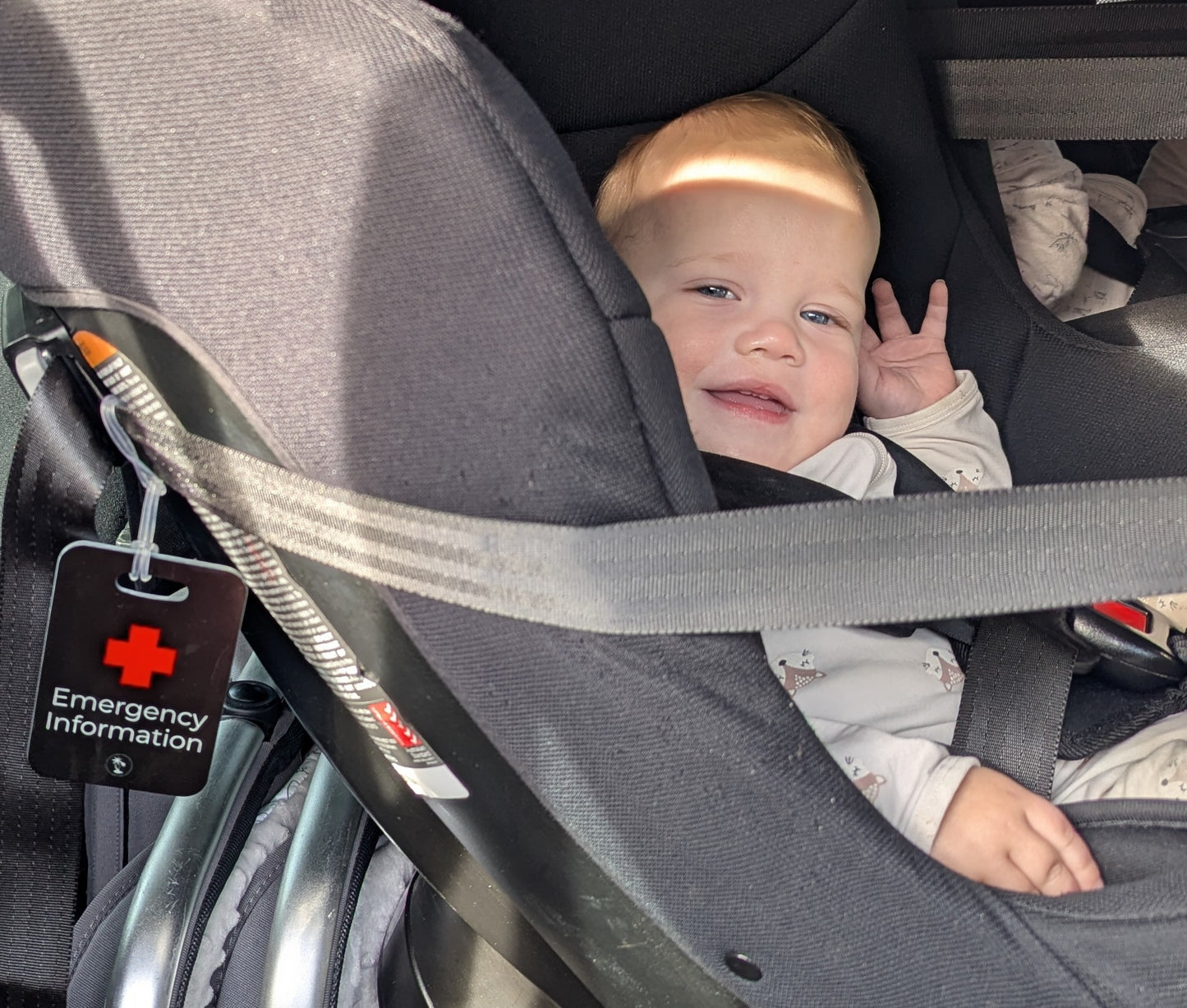 Colour image of Black Hands Here Emergency Medical Information Tag attached to rear facing car seat with smiling baby