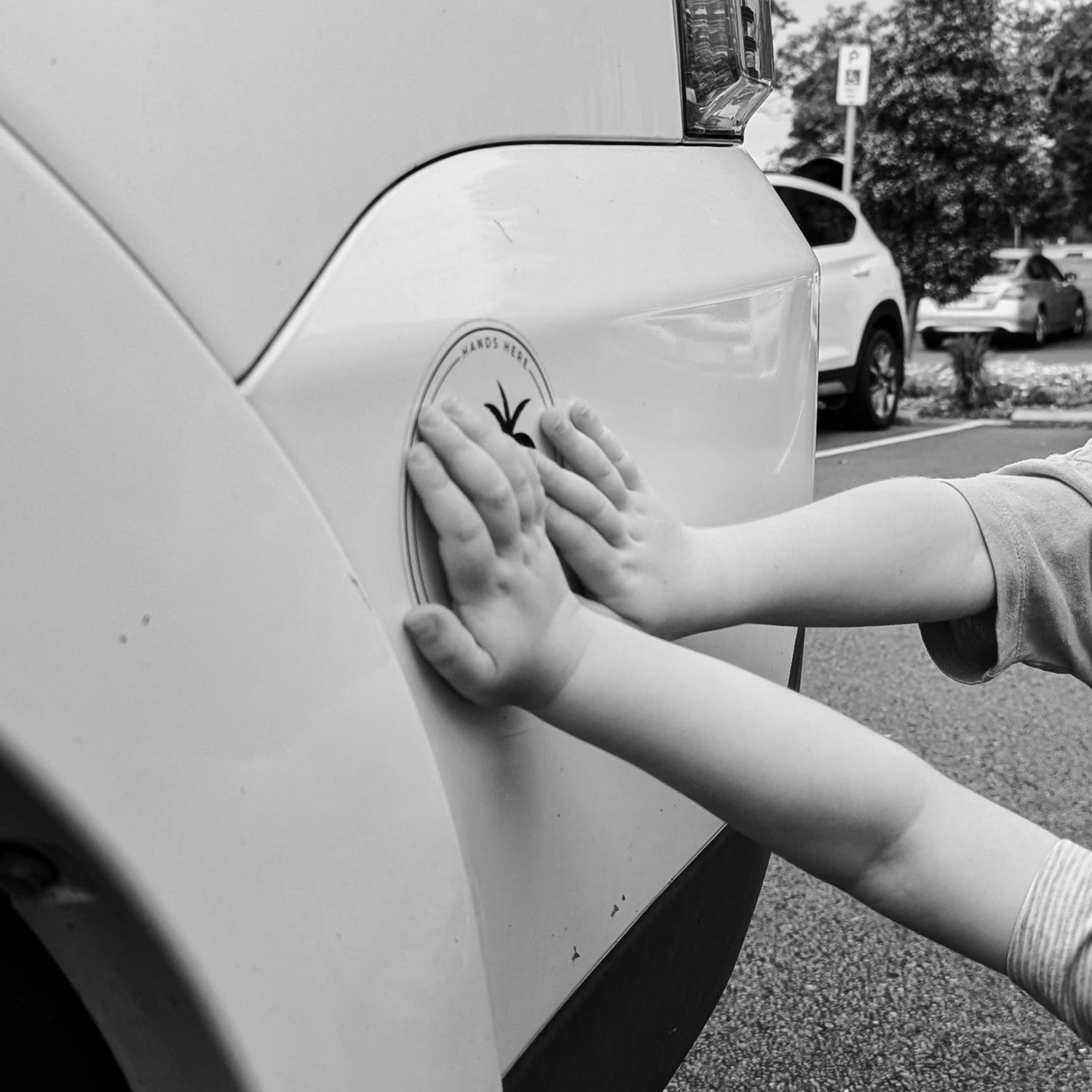 Black and white image of hands of children on Hands Here white palm safety magnet towards the back of vehicle in safe spot