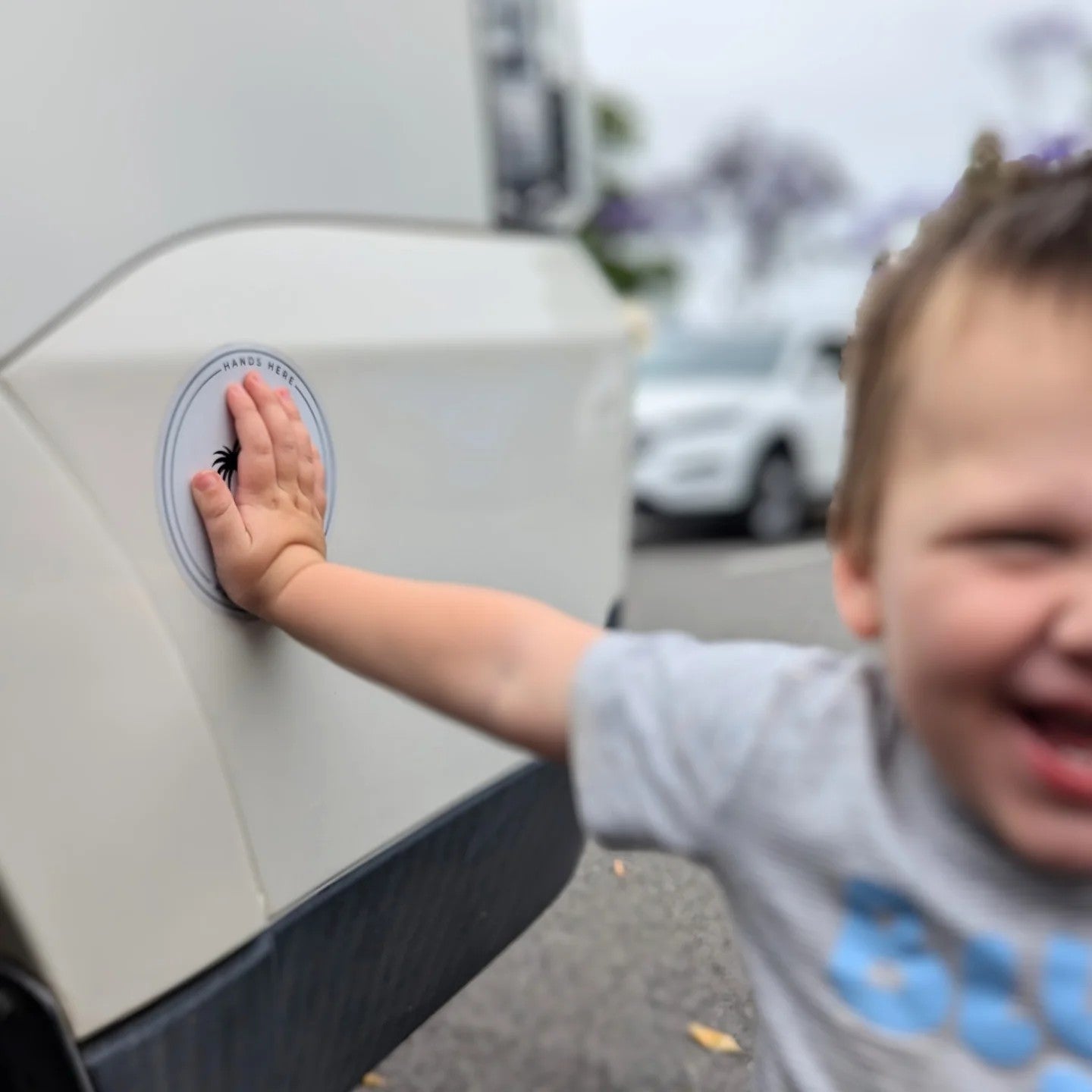Colour image of blurred smiling toddler in safe position facing the camera with his hand on the in focus white palm decal adhered to the vehicle.