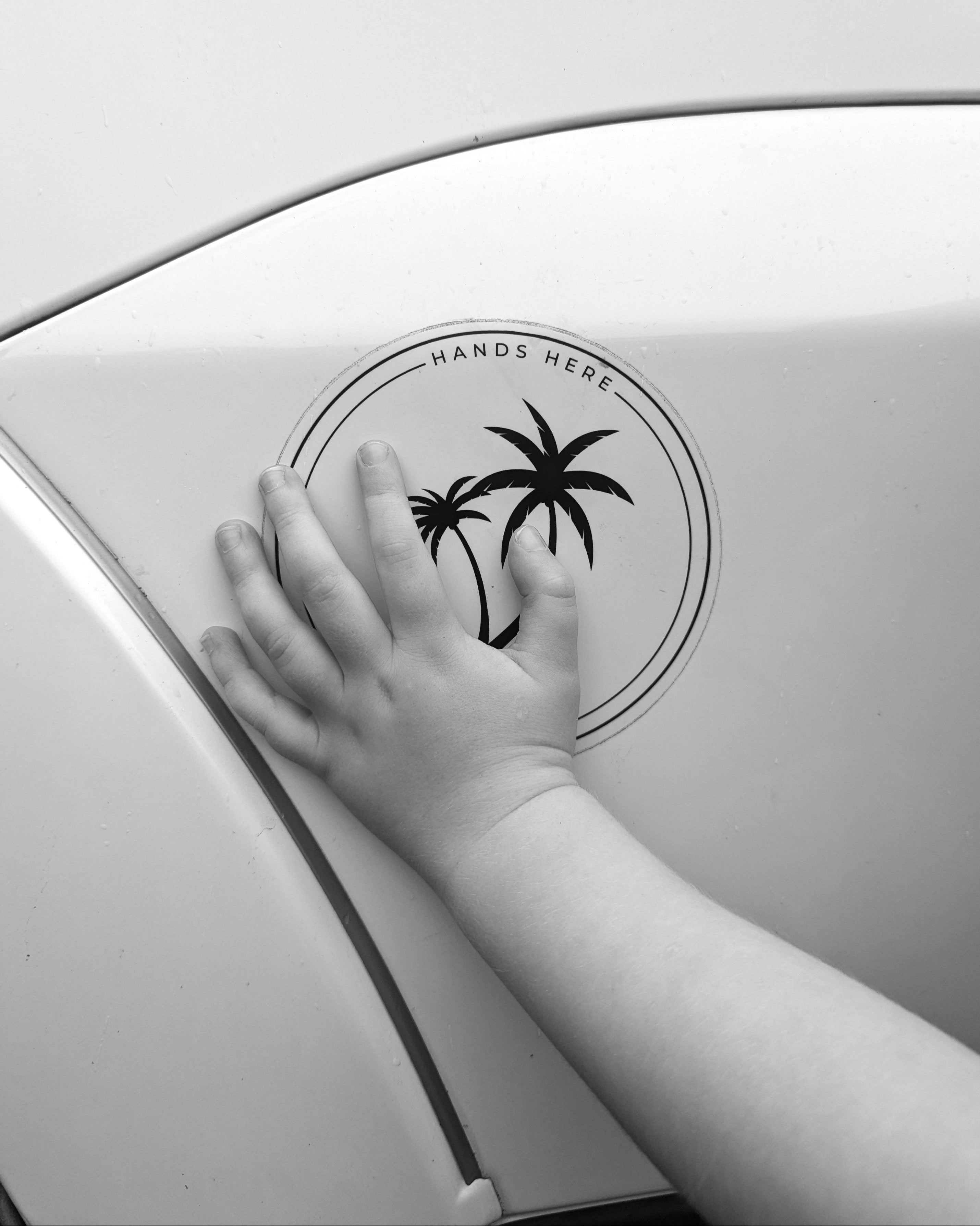 Black and white image of toddler hand on the white palm Hands Here decal, safe and stationary near the vehicle.