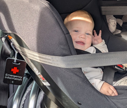 Colour image of Black Hands Here Emergency Medical Information Tag attached to rear facing car seat with smiling baby